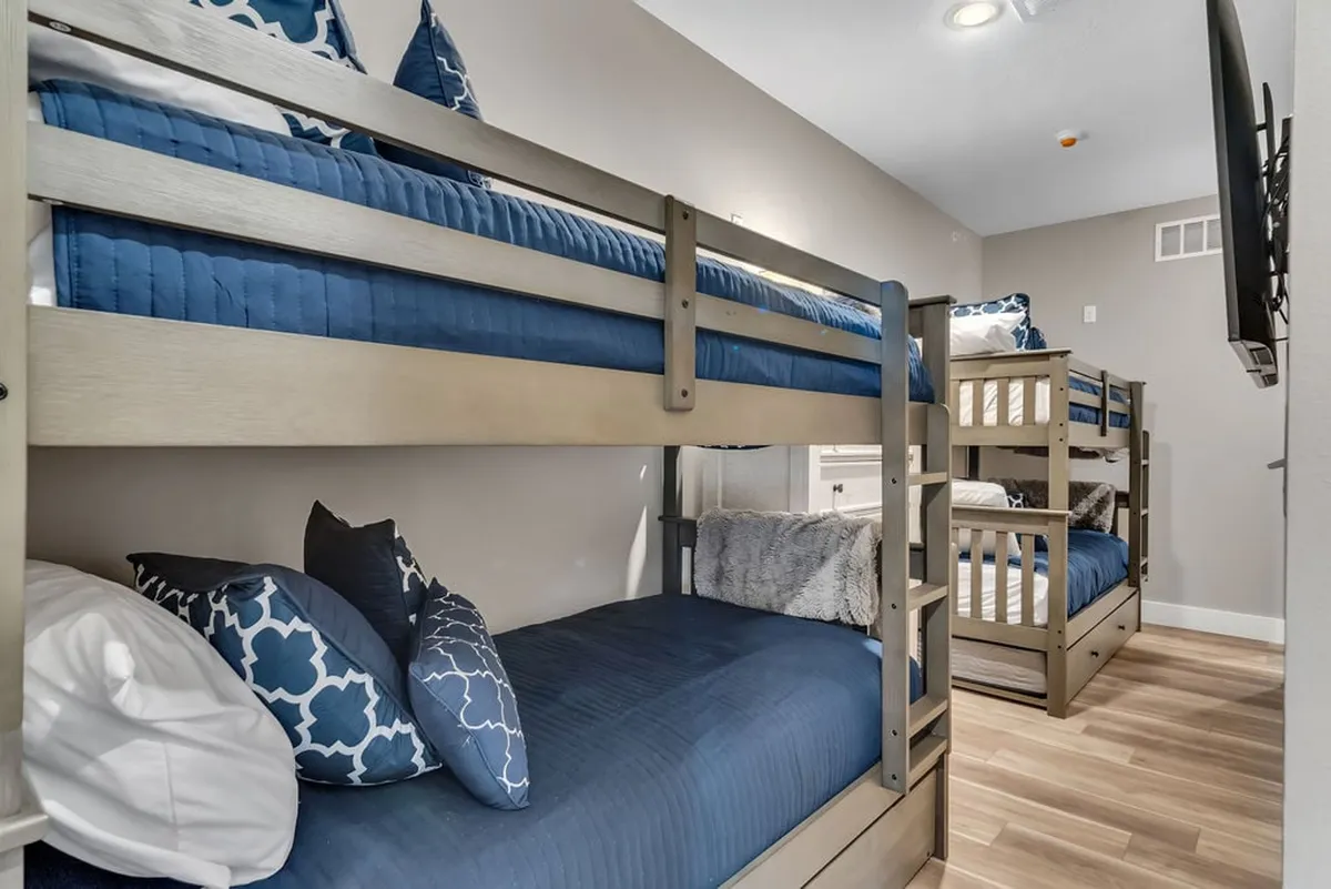 A playful bunk room with cozy bunk beds, each dressed with decorative pillows and soft throws, inviting both relaxation and fun. The space feels vibrant and welcoming—perfect for kids or teens enjoying sleepovers and late-night storytelling.