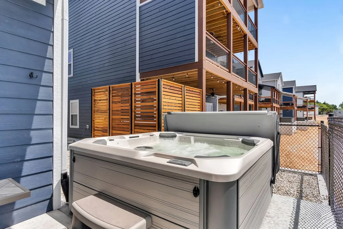 An outdoor scene showing a private hot tub bordered by a wooden privacy screen and the blue siding of the house. The setting is tranquil, ideal for unwinding under the stars after an evening of games.