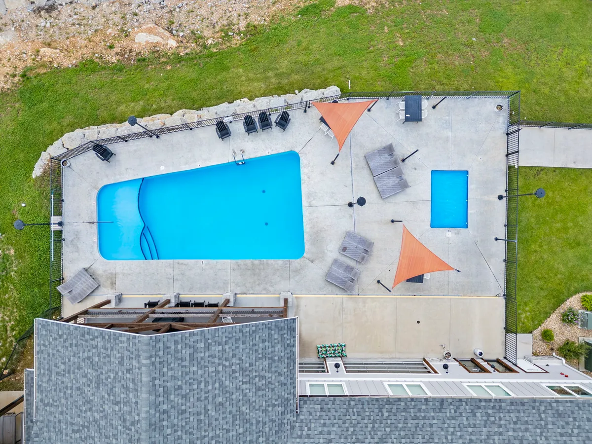 A sparkling outdoor swimming pool surrounded by lounge chairs and shade sails, set within a fenced area. The inviting poolside environment signals resort-style amenities and opportunities for relaxation, sunbathing, and socializing in a high-end setting.