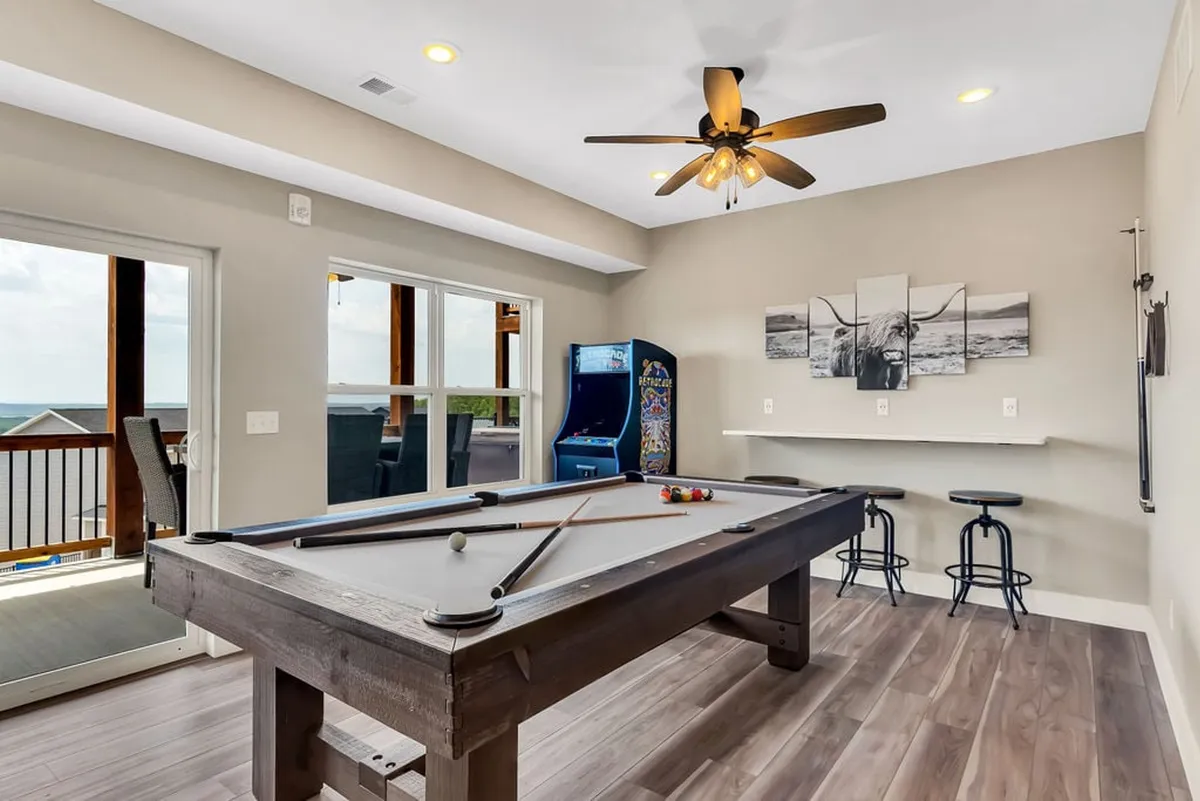 This image captures a vibrant game room scene featuring a pool table, a vintage arcade machine, bar stools, and artwork on the wall. The space exudes a playful and casual atmosphere, perfect for friendly competitions and group fun.