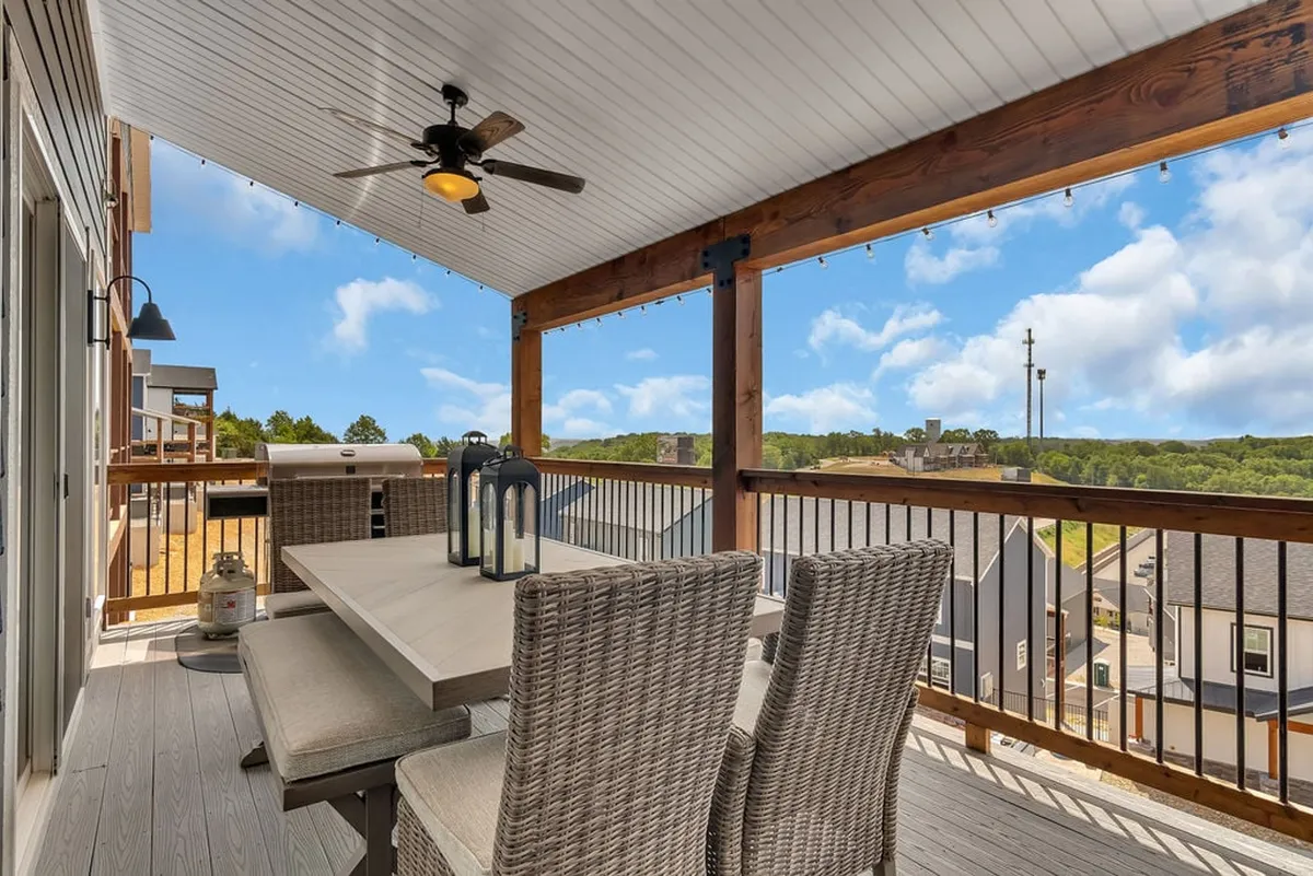 An outdoor deck with a large dining table, ceiling fan, and sweeping landscape views beyond. The casual seating arrangement invites guests to enjoy meals or drinks together while taking in the natural beauty that surrounds the lodge.