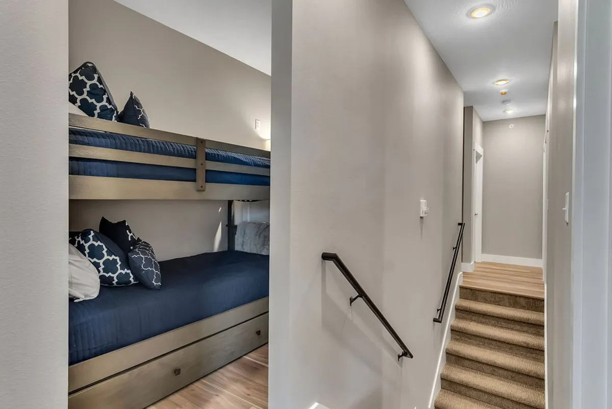 A cozy bunk room with sturdy wooden bunks, decorative pillows, and an integrated staircase. The inviting setup encourages family bonding, bedtime stories, and creates a memorable sleepover environment.