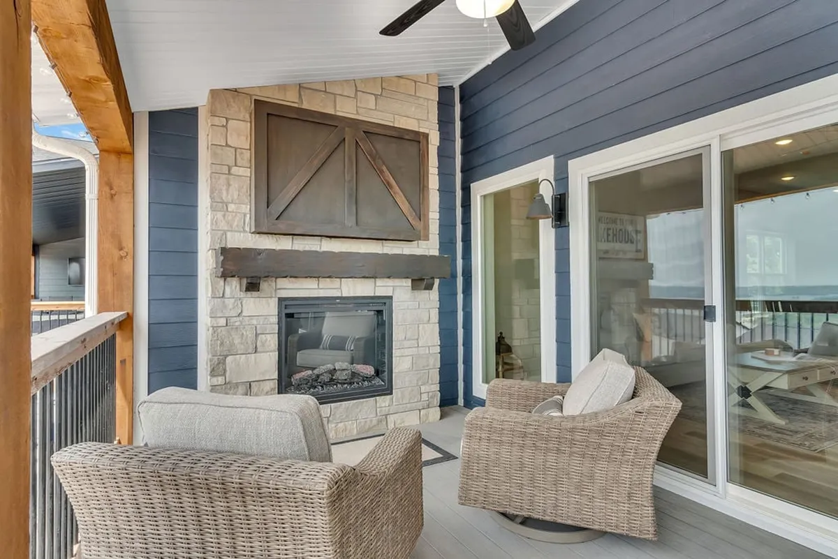 An inviting exterior lounge area with a prominent stone fireplace, comfortable wicker chairs, and rustic wooden beams. The setup overlooks scenic views, suggesting a perfect setting for cozy autumn evenings or spring sunsets.