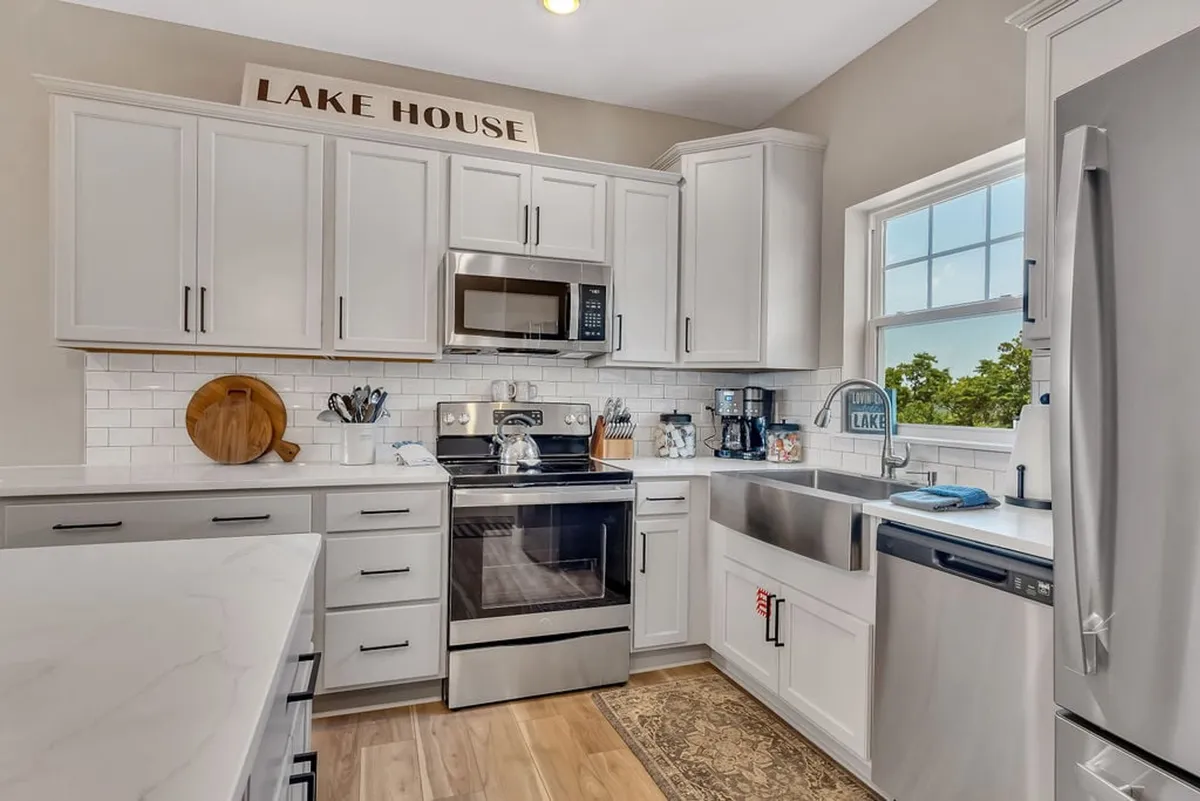 A gourmet kitchen featuring elegant cabinetry, stainless steel appliances, marble countertops, and a window above the sink providing views outside. A 'Lake House' sign adds a cozy, personalized touch, making the kitchen feel like the heart of the home.