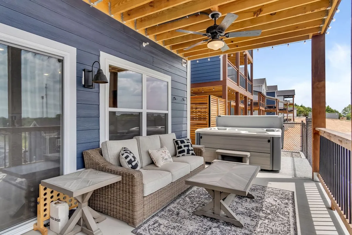 An exterior patio area with a cozy outdoor sofa, a hot tub, wooden ceiling, and decorative pillows, suggesting a seamless blend of indoor comfort and outdoor enjoyment. The space is ideal for lively conversations, stargazing, or unwinding after games.