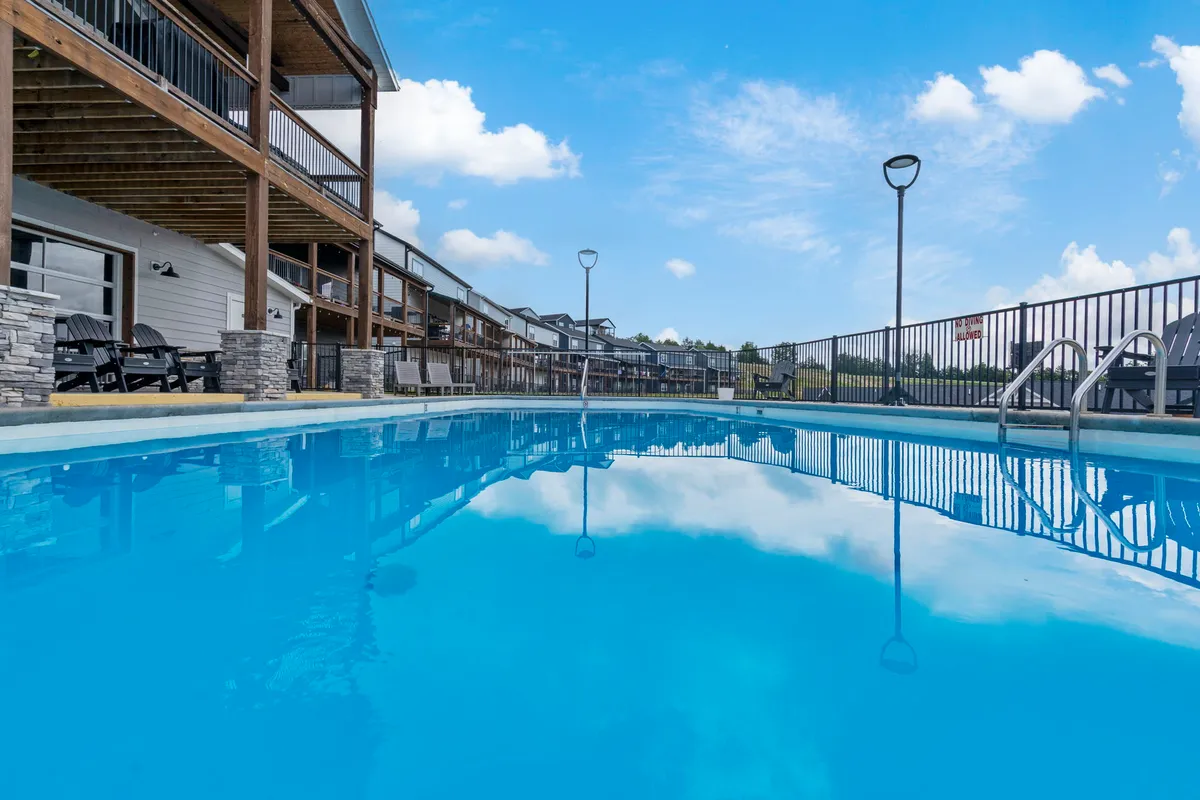 This exterior image features a sparkling swimming pool surrounded by a spacious deck area, with the lodge buildings and an open sky in the background. The pool area is set up for both relaxation and socializing, ideal for sunny summer days or evening gatherings.