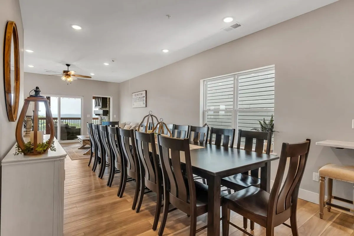 A long farmhouse dining table set next to large windows, with a decorative lantern as a centerpiece. The spacious seating is ideal for family meals and celebrations, and the ample natural light highlights the communal, welcoming ambiance.