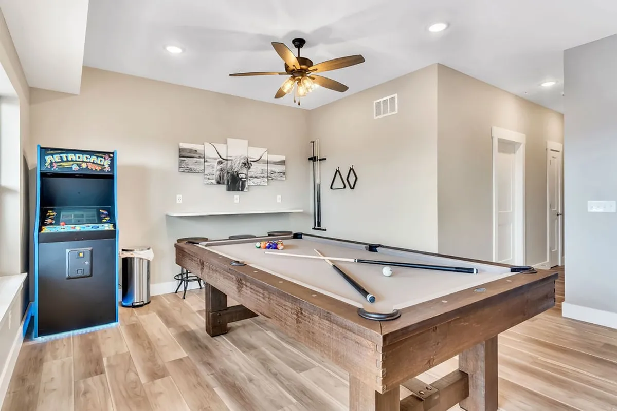 A lively interior game room featuring a pool table, arcade machine, ceiling fan, and vibrant wall art. The space is designed for friendly competition and socializing, creating a fun atmosphere for game nights and family laughter.