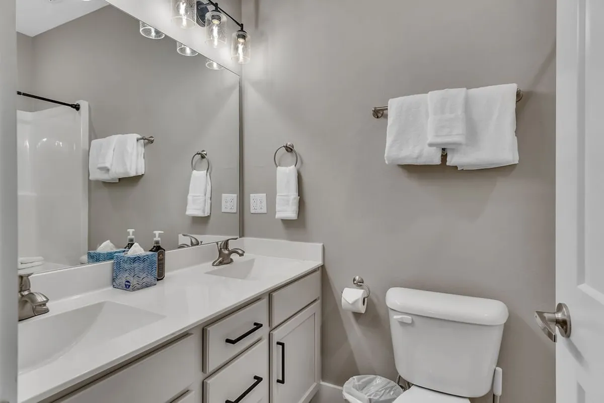 A fresh, light-filled bathroom featuring a double vanity, large mirror, modern industrial light fixtures, and crisp white towels. The clean, spa-like ambiance suggests both practicality and luxury for guest routines.